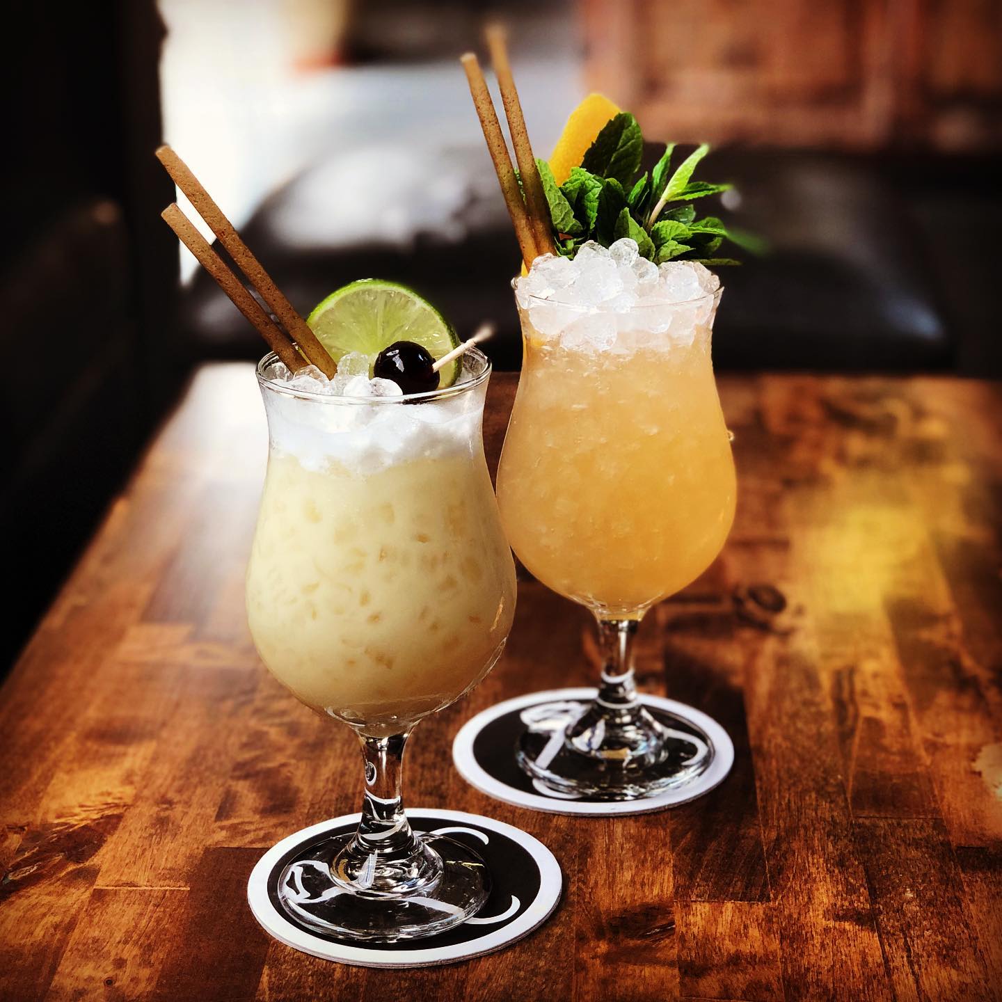 Two garnished cocktails sitting on Prizefighter Bar coasters