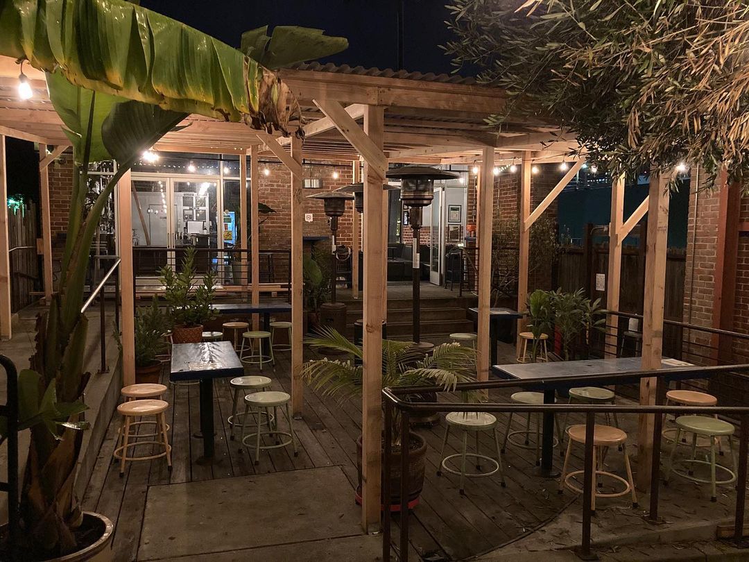 Photo of Prizefighter Bar's patio, with bench seats, high tops tables, space heaters, plants, and pleasant evening lighting.